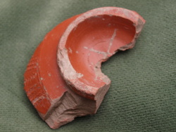 Fragmento de la base de un plato de terra sigillata (tipología de Mezquiriz) engobada en color rojo. El pie es anular de sección triangular, con una cruz de reducidas dimensiones de la que se conservan dos pequeños brazos y el arranque de los otros dos