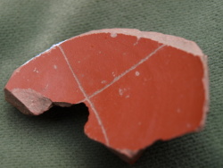 Fragmento de la base de un plato de terra sigillata (tipología de Mezquiriz) engobada en color rojo. En el interior del plato se aprecian una cruz incisa con tres brazos y el arranque de un cuarto. La cruz cubriría buena parte del interior