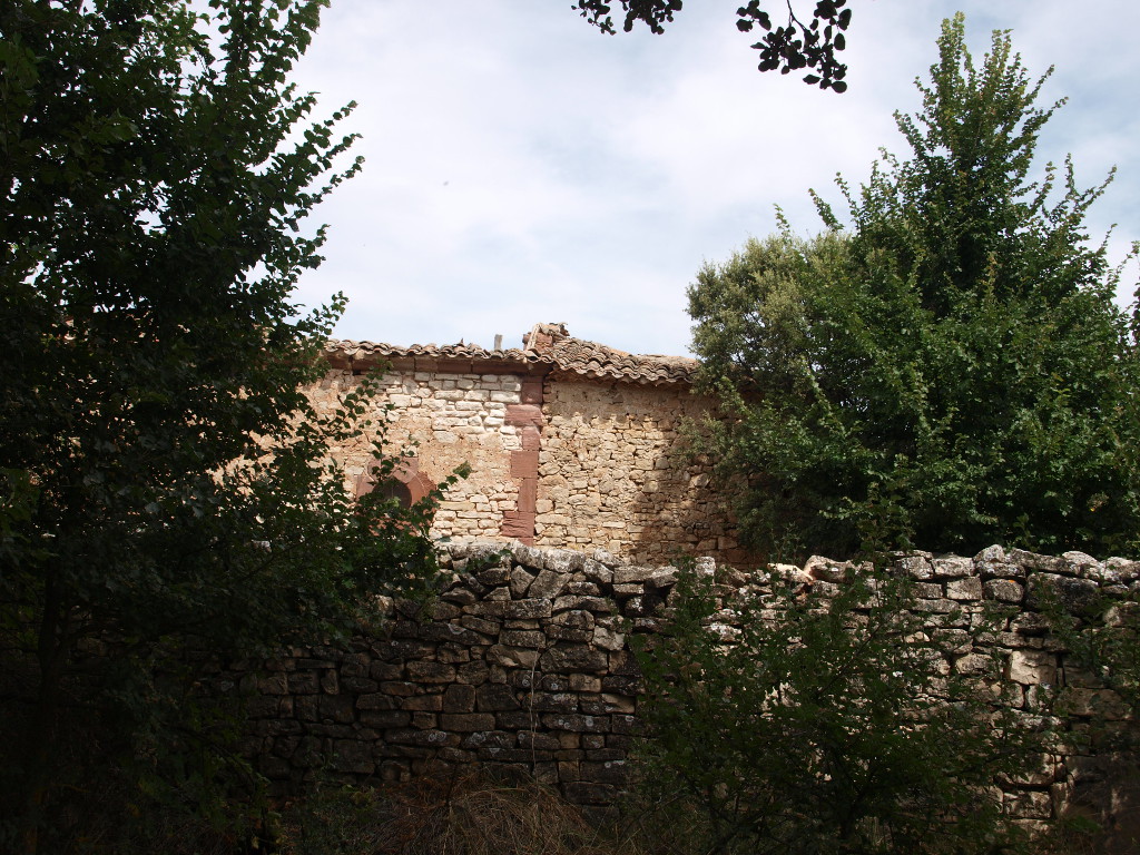 La cabecera de la ermita, tal y como se la adivina a través del arbolado y la valla del cementerio que la rodea parcialmente