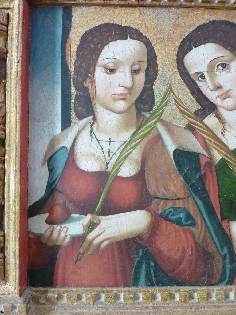Una atractiva joven de pelo castanño, mirada esquiva y vestido escotado sostiene en su mano izquierda una palma y en la derecha una bandeja con un corazón